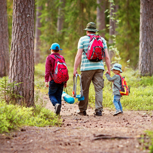 Erwachsener mit zwei Kindern auf einem Waldweg. Alle tragen Wanderausrüstung. Link zur Kartenanwendung Wanderwege in Lippe.